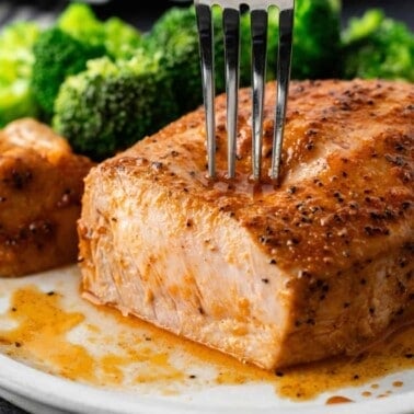 A seasoned baked pork chop on a plate with a slice removed.